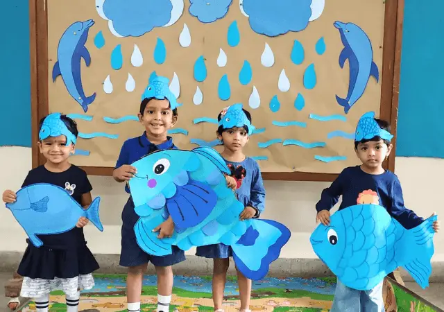 a group of children of class Nursery of Ashish Preschool holding blue fish during rainy day activity